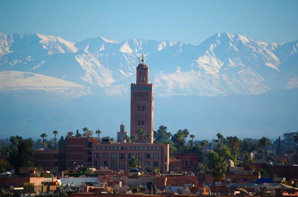 View of the Koutoubia Mosque with the Atlas Mountains in the background, showcasing a clear sky and snow-capped peaks.