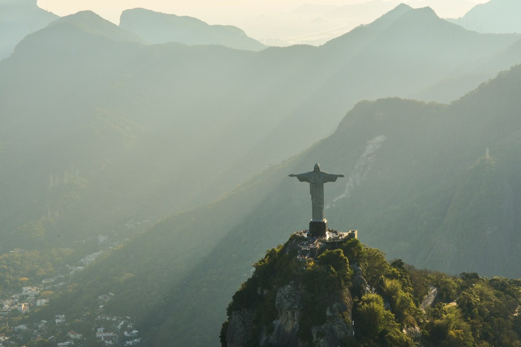 Aerial view of the Christ the Redeemer statue atop a mountain, surrounded by misty hills in Rio de Janeiro, Brazil.