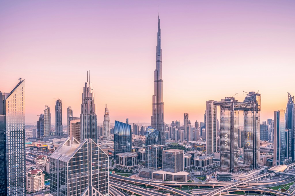 A panoramic view of Dubai's skyline at sunset, featuring the iconic Burj Khalifa soaring above modern skyscrapers and a vibrant sky.